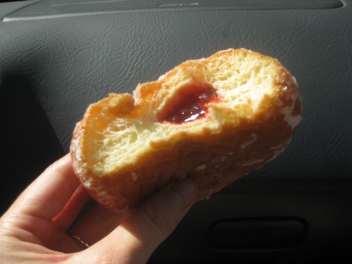 Hand holding raspberry filled vegan donut.