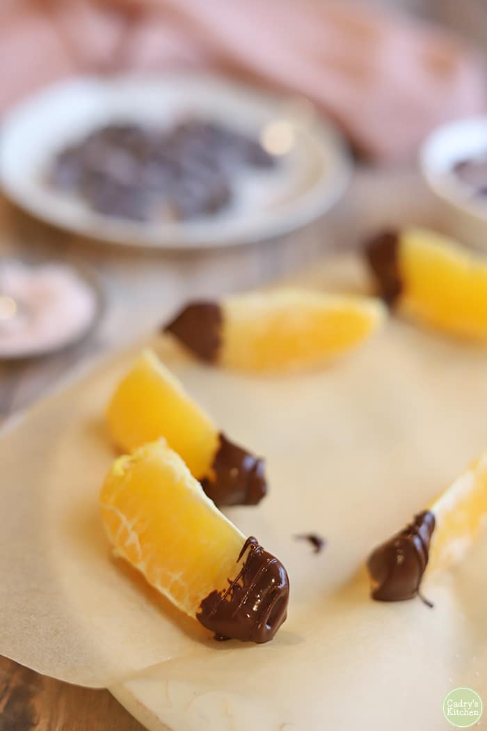 Orange slices on parchment paper covered plate dipped in chocolate.