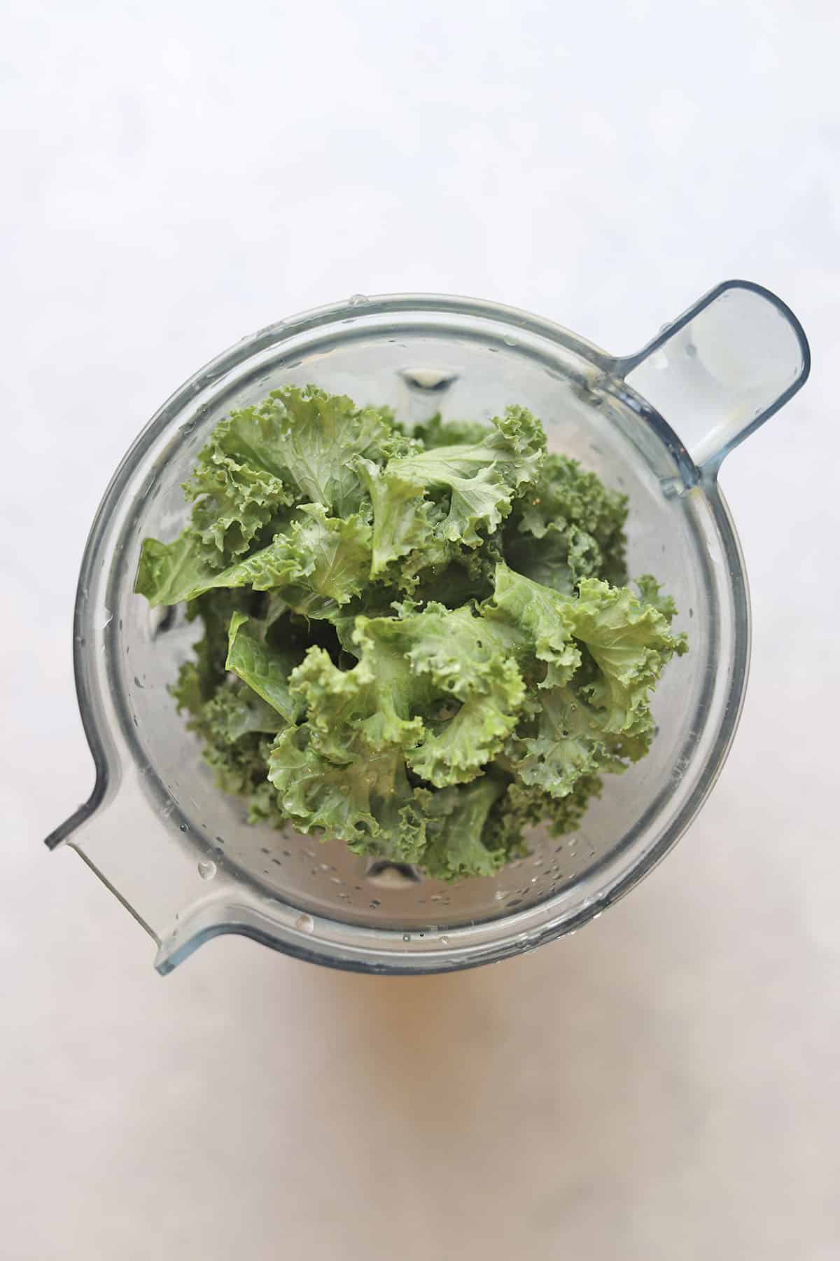 Overhead blender with raw kale and other smoothie ingredients.