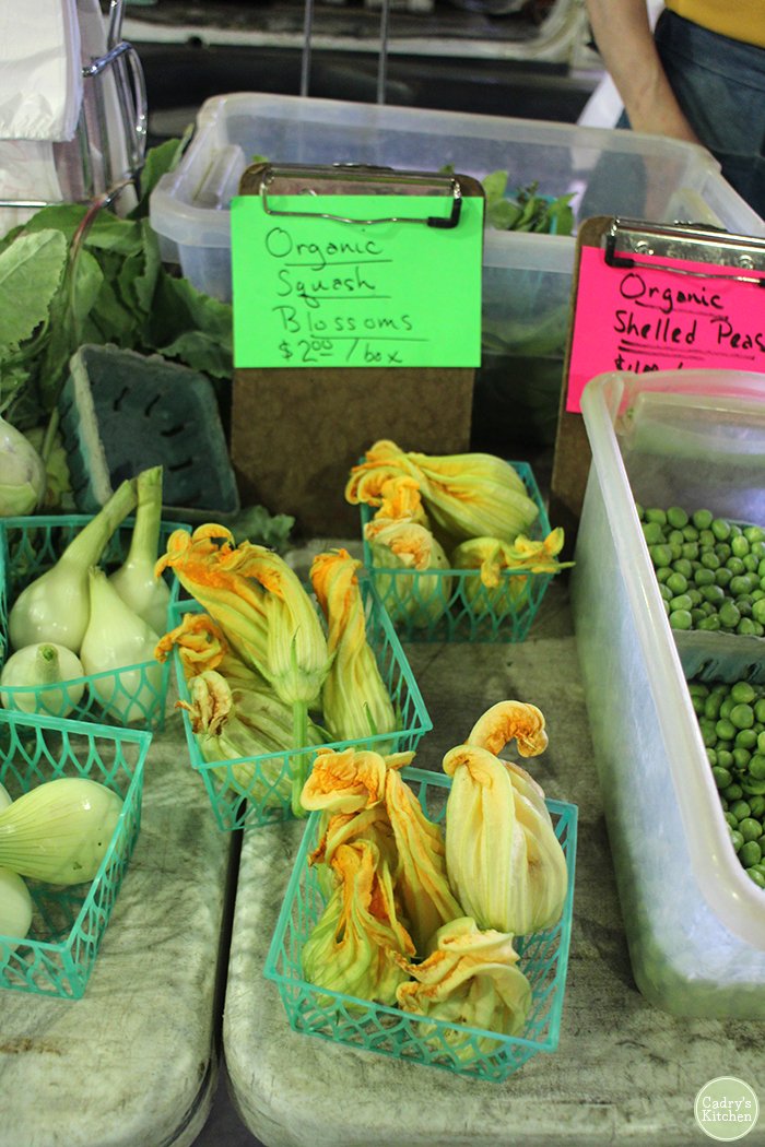 Squash blossoms on table at farmers market in plastic boxes.