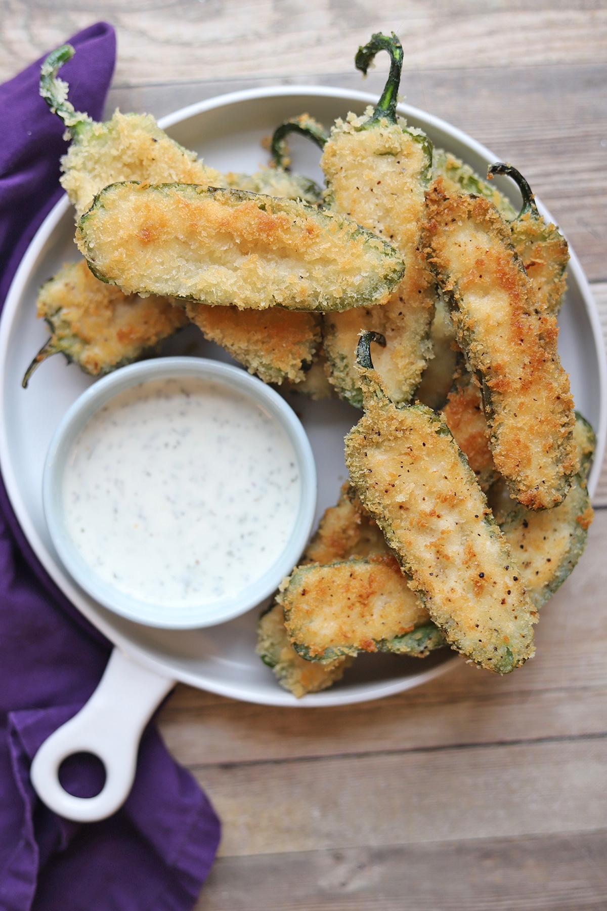 Vegan jalapeno poppers on platter with bowl or ranch dressing.