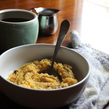 Creamy polenta in bowl with sun-dried tomatoes. Cup of coffee & creamer pitcher in background.