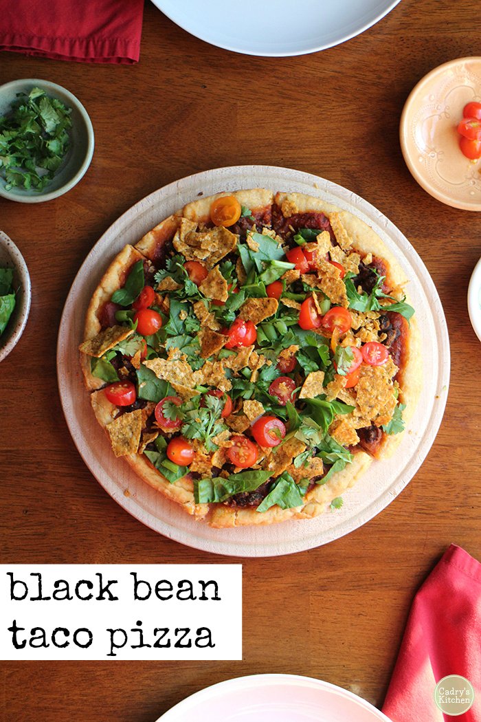 Text overlay: Black bean taco pizza. Pizza on table with toppings and red napkin.