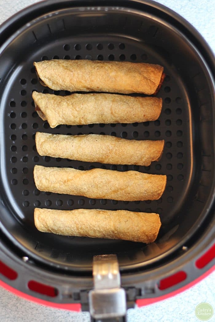 Overhead baked taquitos in air fryer basket.