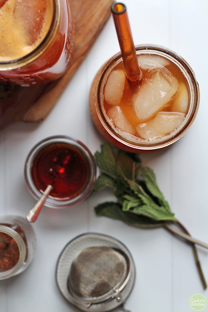 Overhead glass of red rooibos iced tea, loose rooibos, and tea ball on table.