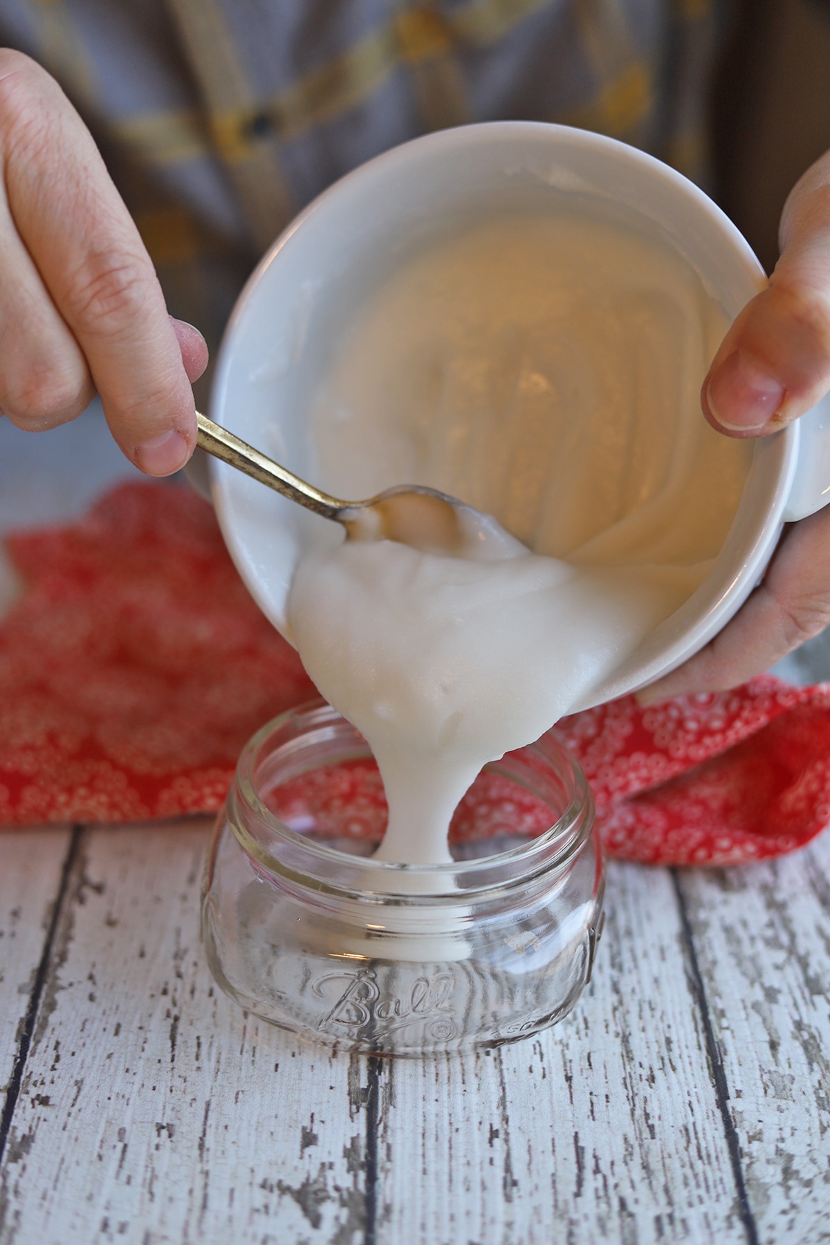 Pouring coconut oil deodorant from bowl into clean jar.