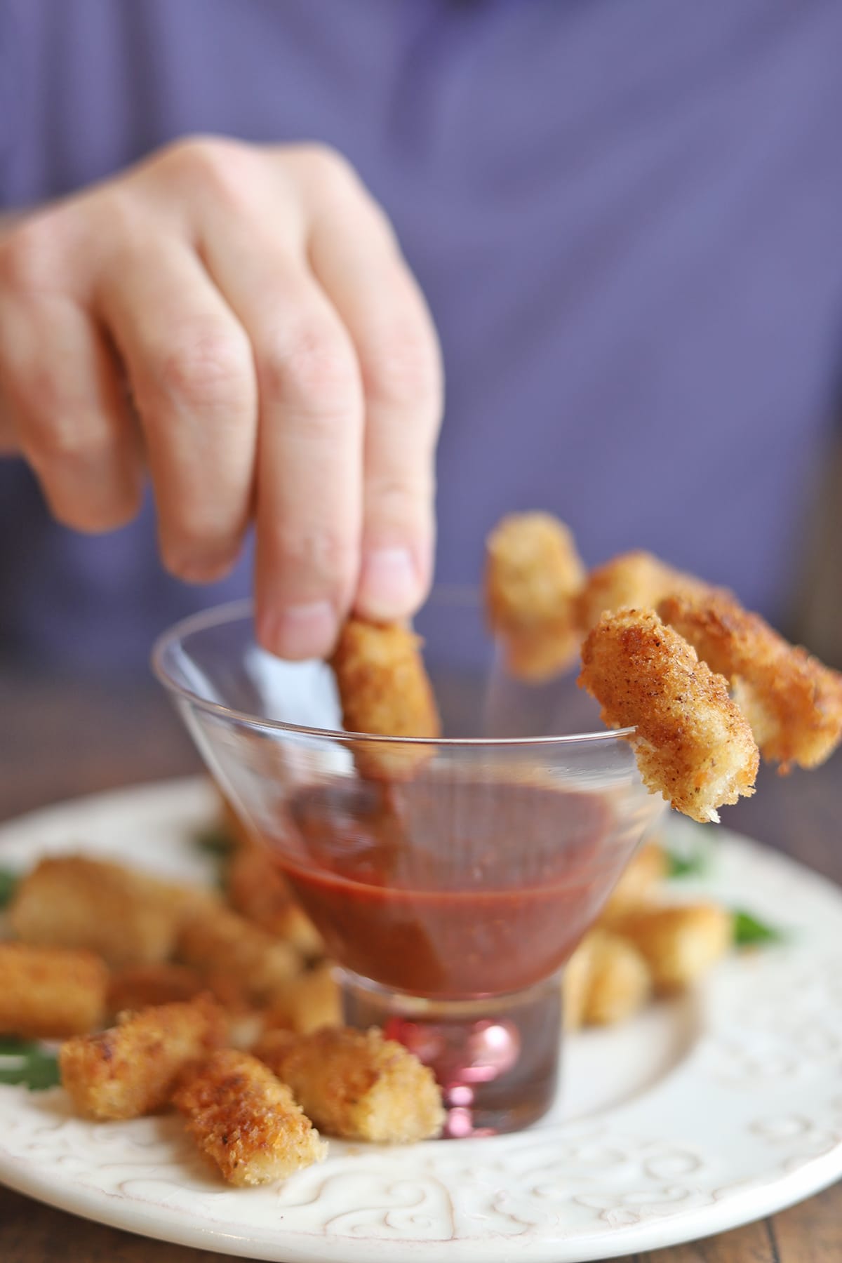 Hand dipping breaded hearts of palm into sauce.