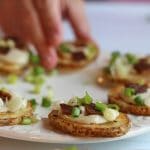 Sliced roasted potatoes with cashew cream, seitan bacon, and green onions on platter.