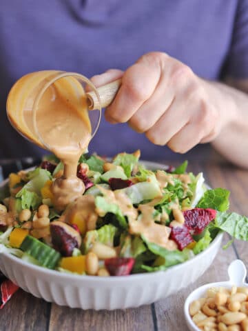 Hand pouring peanut dressing onto salad.