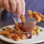 Hand dipping breaded vegan shrimp into cocktail sauce.