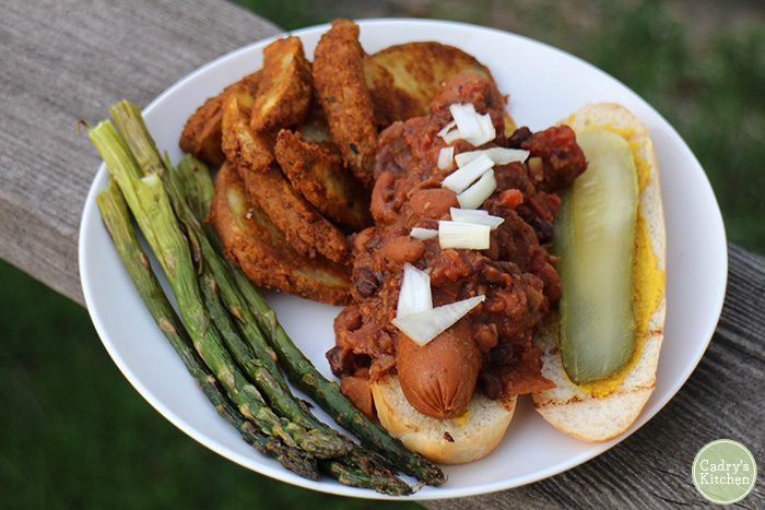 Chili dog on plate with potatoes and asparagus.