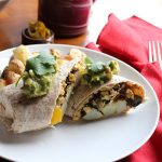 Breakfast burrito on plate by red napkin.