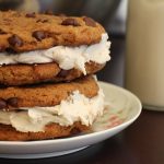 Chocolate chip cookies stacked on top of each other with vegan vanilla frosting in between them.