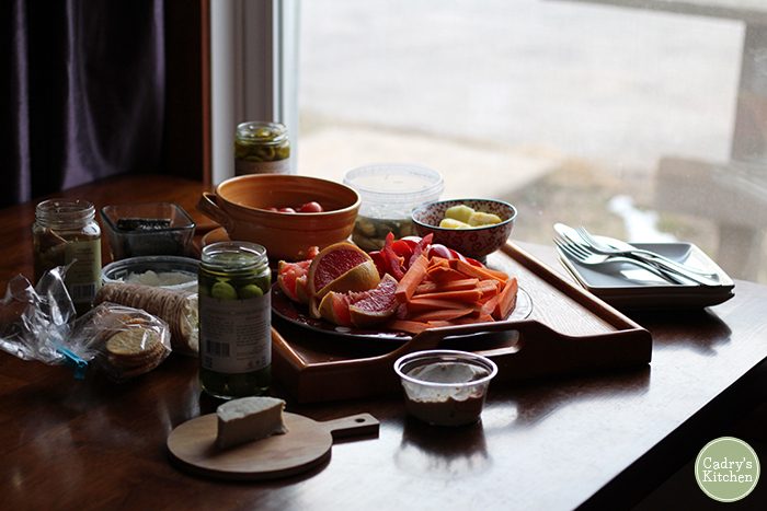 Table loaded with a plethora of jars, vegan cheeses, crackers, and vegetables.