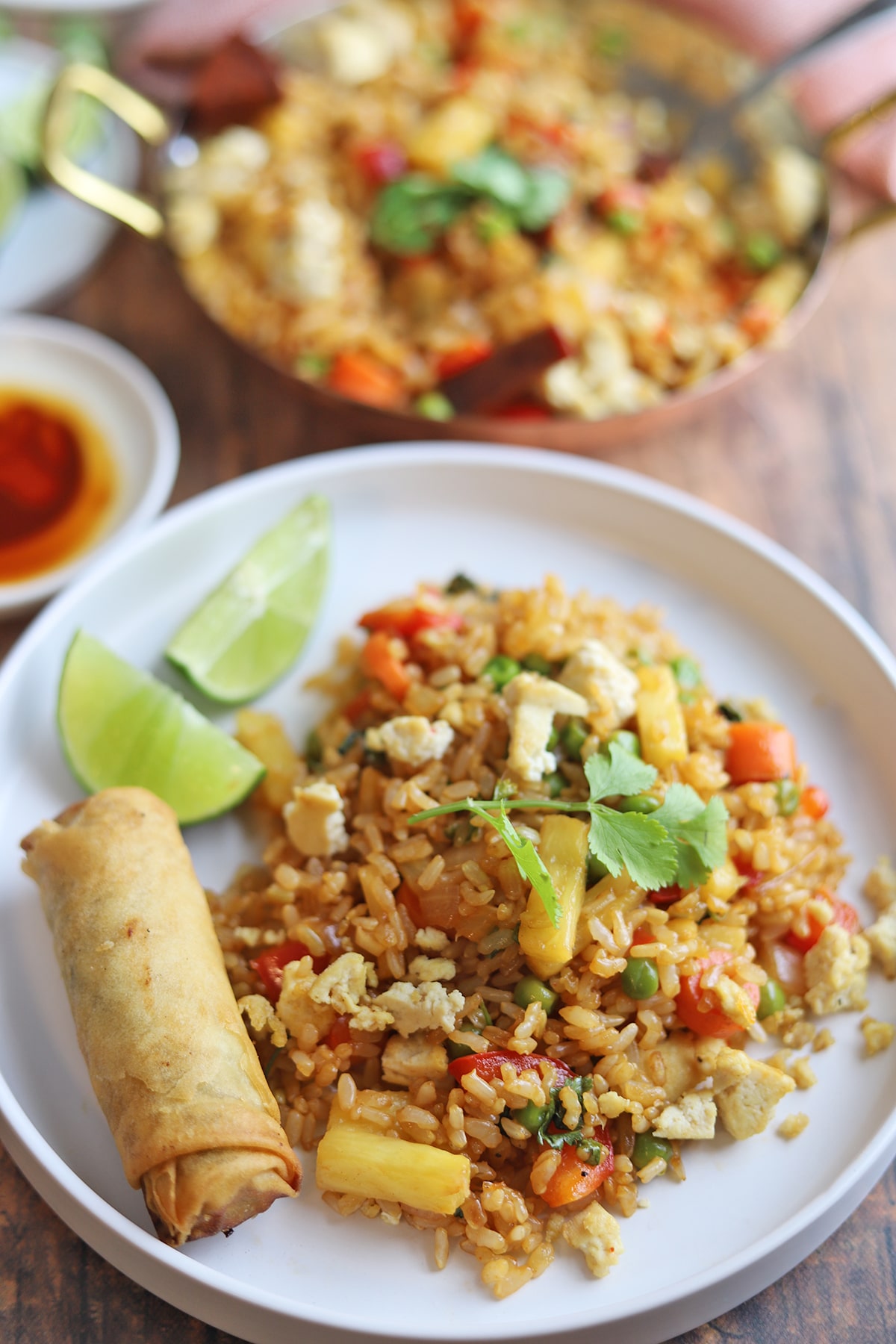 Plate with pineapple fried rice, spring roll, and lime wedges.
