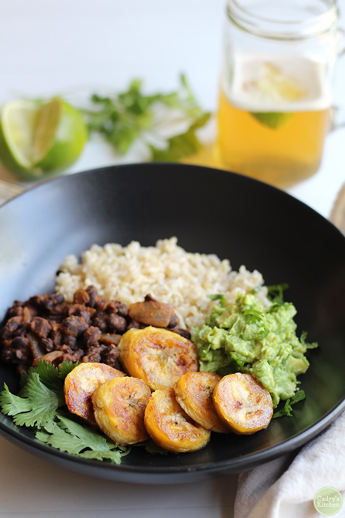 Fried plantains, guacamole, black beans, and rice in black dish.