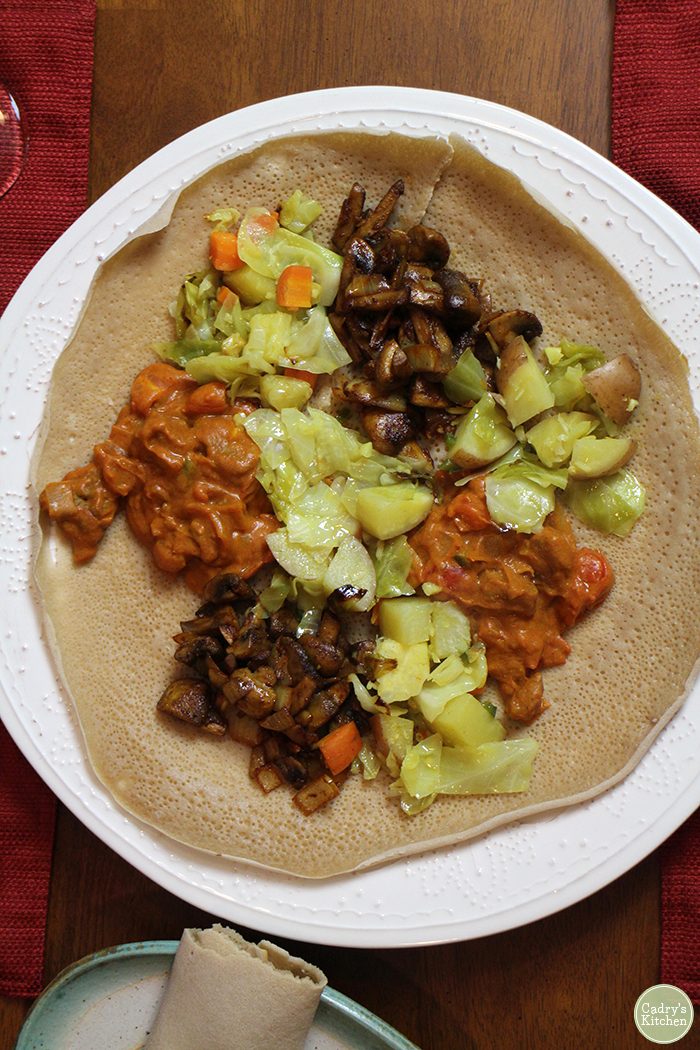 Overhead injera on platter with Ethiopian wots - cabbage, mushrooms, and lentils.