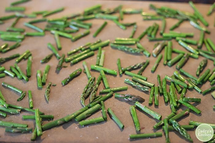 Asparagus pieces on parchment paper covered baking sheet.
