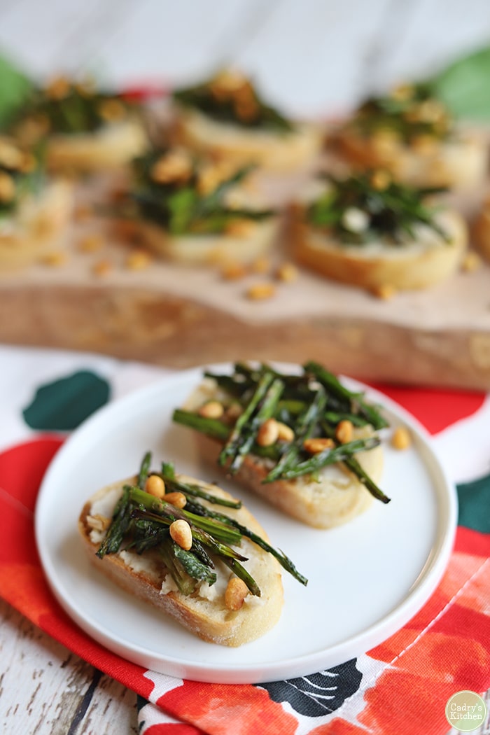Roasted asparagus with pine nuts on toasted baguette on small plate.