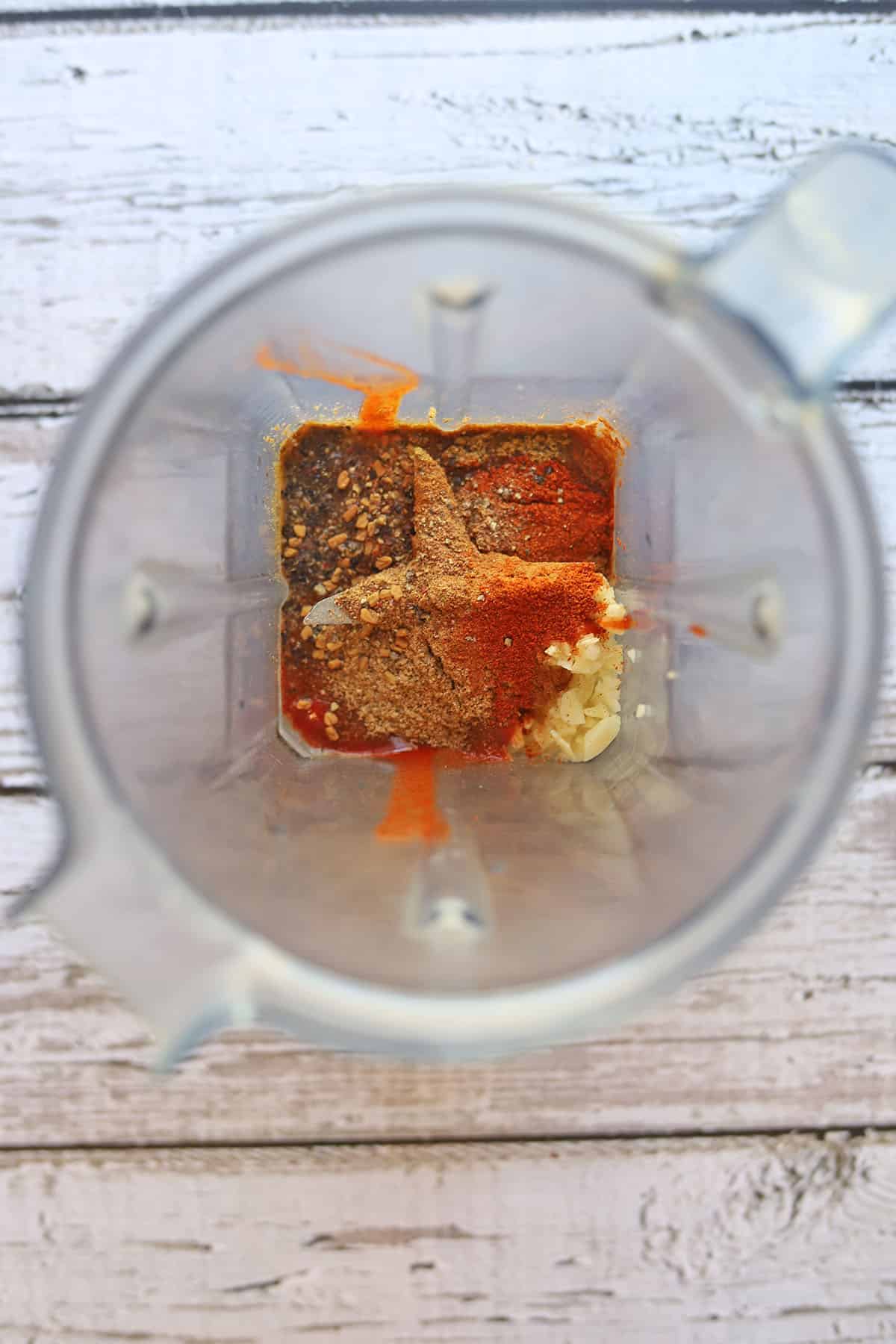 Spices, garlic, and sriracha in blender pitcher.