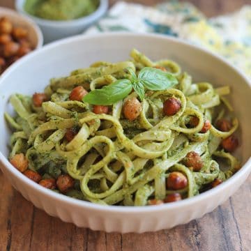 Bowl of pasta on table topped with chickpeas and fresh basil.