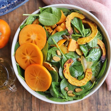 Overhead spinach salad with persimmons and roasted squash in bowl.