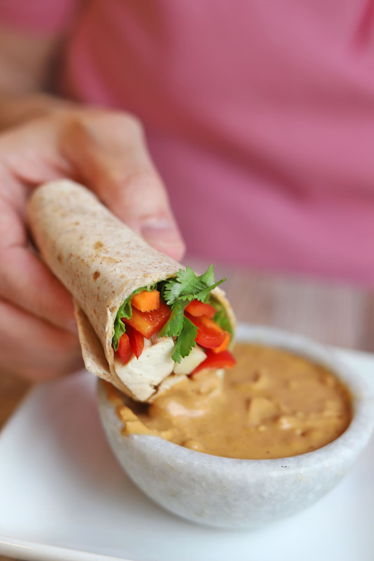 Tortilla wrap being dipped into bowl of peanut sauce.