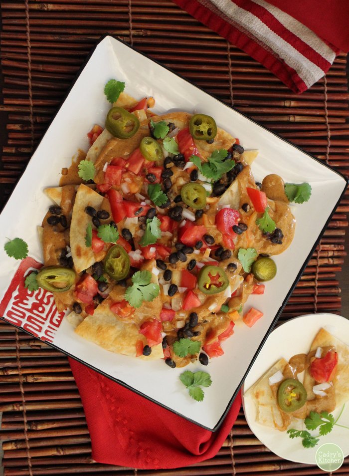 Overhead fried nachos platter with non-dairy queso, black beans, and tomatoes.