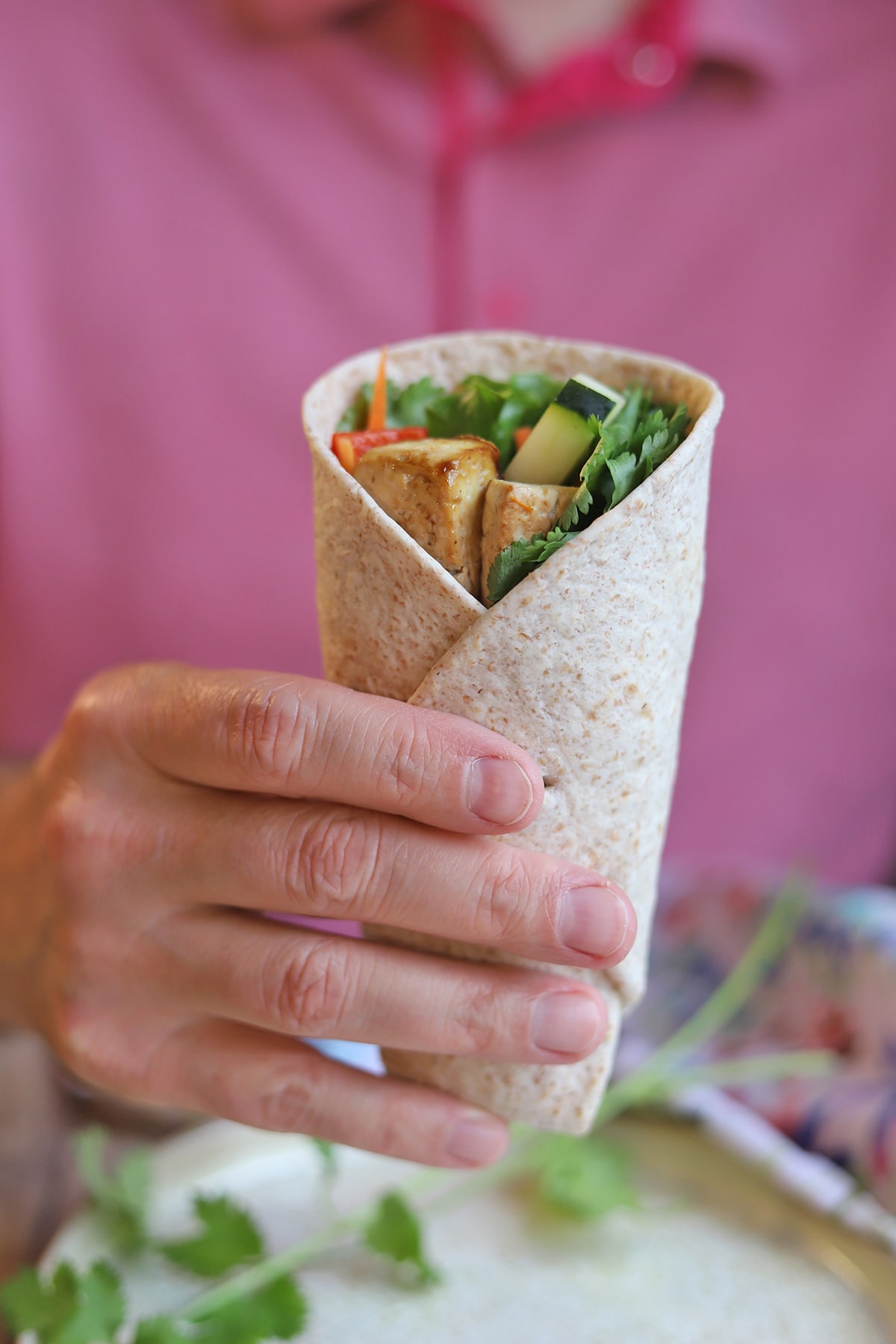 Hand holding wrap with tofu, lettuce, and carrots.