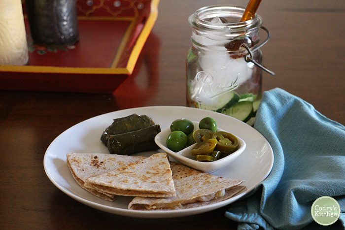 Toasted tortilla wedges with hummus with dolmas, olives, and jalapeno slices.