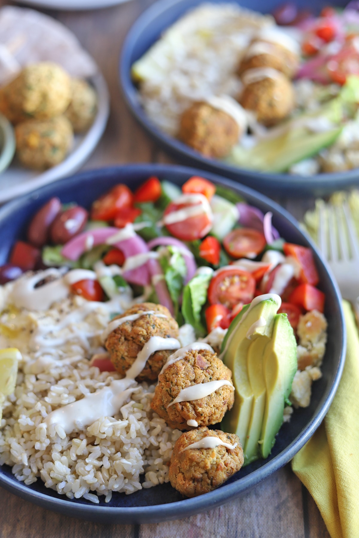 Falafel drizzled with tahini sauce in salad and rice bowl.