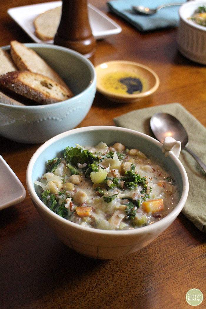 Chickpea and rice soup with kale in bowl by bread & olive oil.