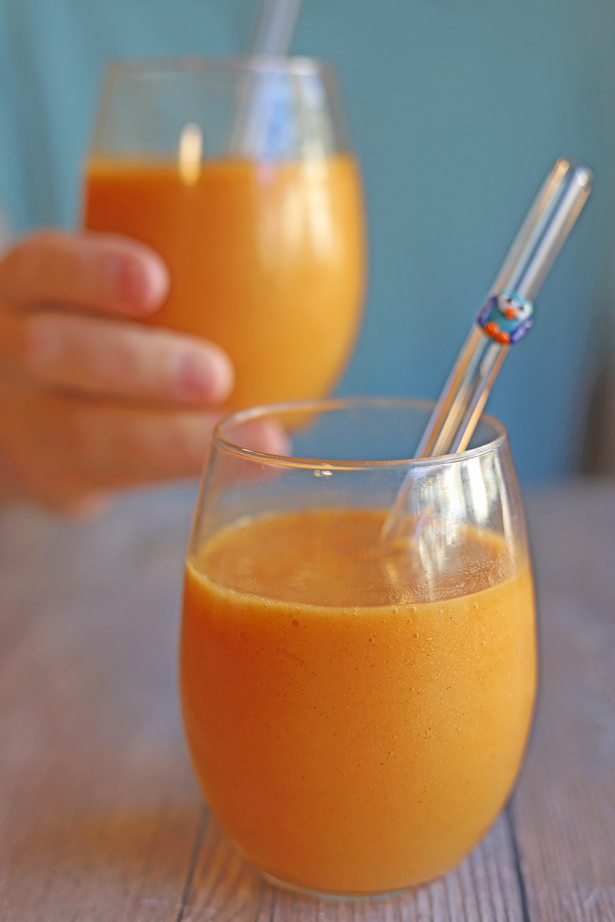 Sweet potato smoothie in glass with straw, hand holding glass in background.