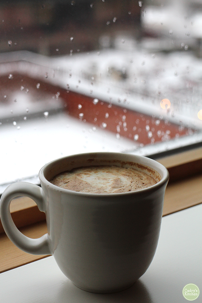 Coffee mug by window with rain on it.