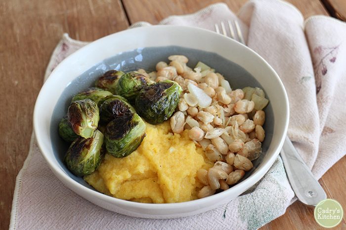 Polenta in bowl with Brussels sprouts and white beans.