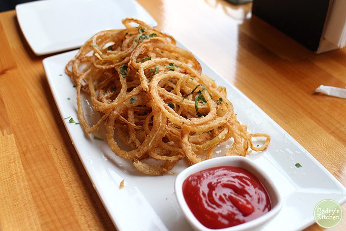 Thinly sliced onion rings with ketchup on plate.
