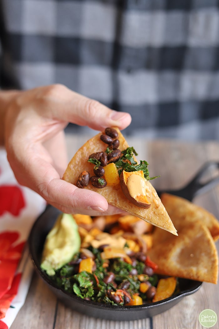 Hand holding fried tortilla wedge with sweet potato black bean hash.