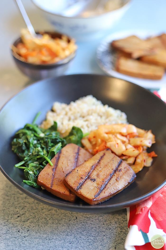 Grilled marinated tofu in bowl with sauteed spinach, brown rice, and kimchi.