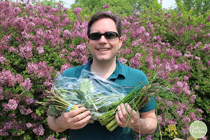 David holding an armful of vegetables in front of flowers.