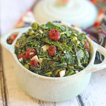 Collard greens cooked with garlic and cranberries in serving dish.