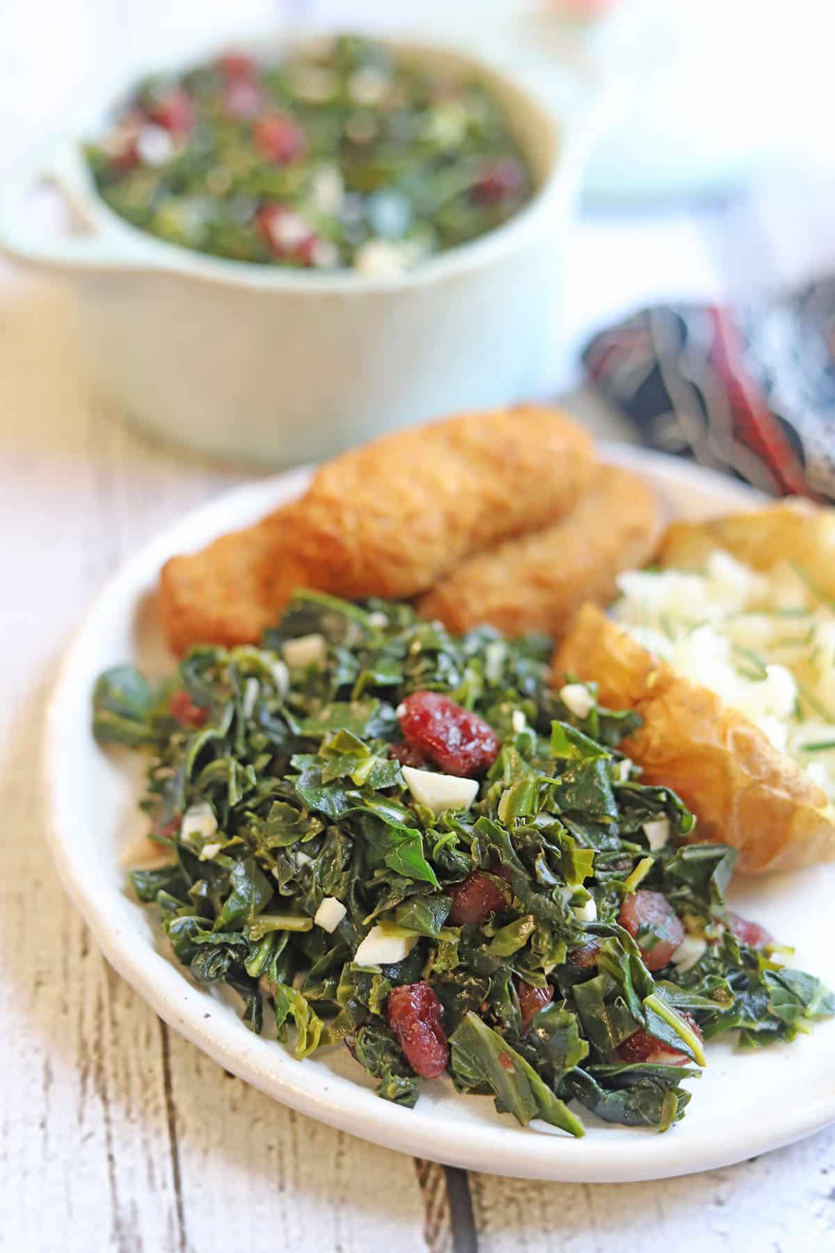 Collard greens with cranberries on plate by baked potato and vegan chicken strips.