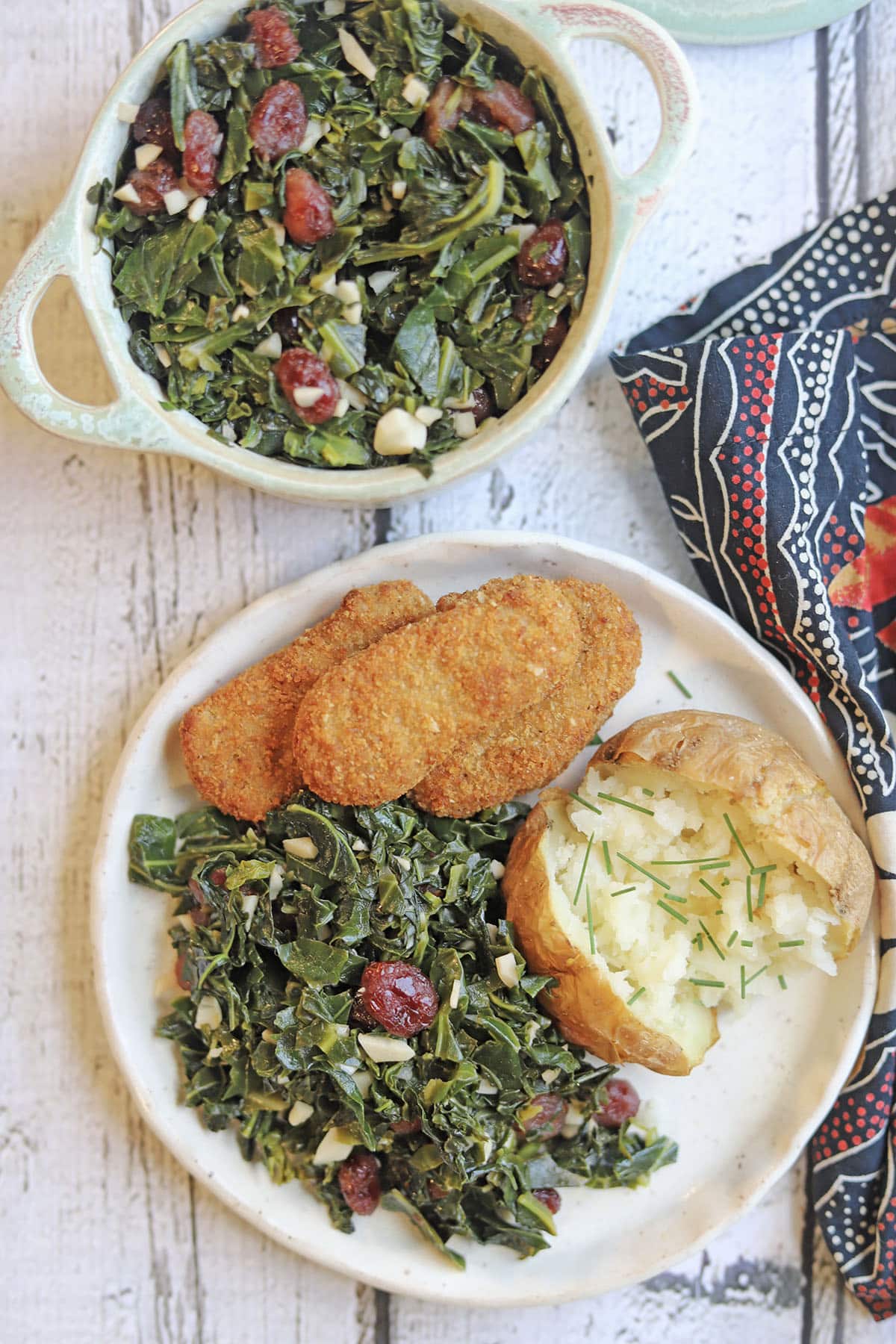 Overhead plate with vegan chicken strips, collard greens, and baked potato.