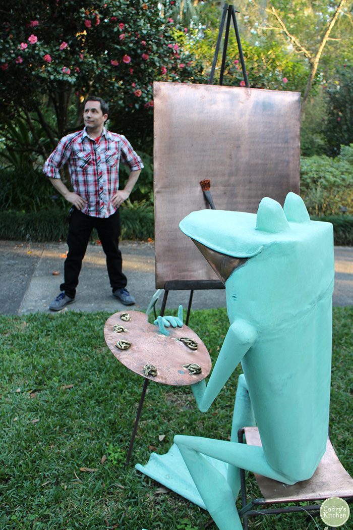 David posing for frog sculpture, who appears to be painting.