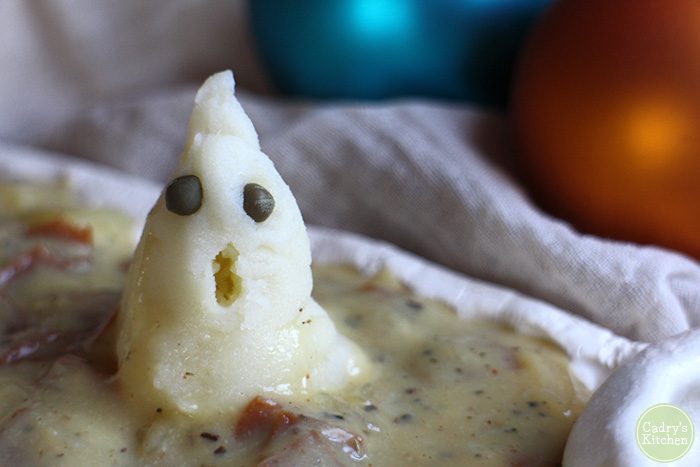 Close-up mashed potato ghost with caper eyes sitting on seitan bacon vegan gravy.