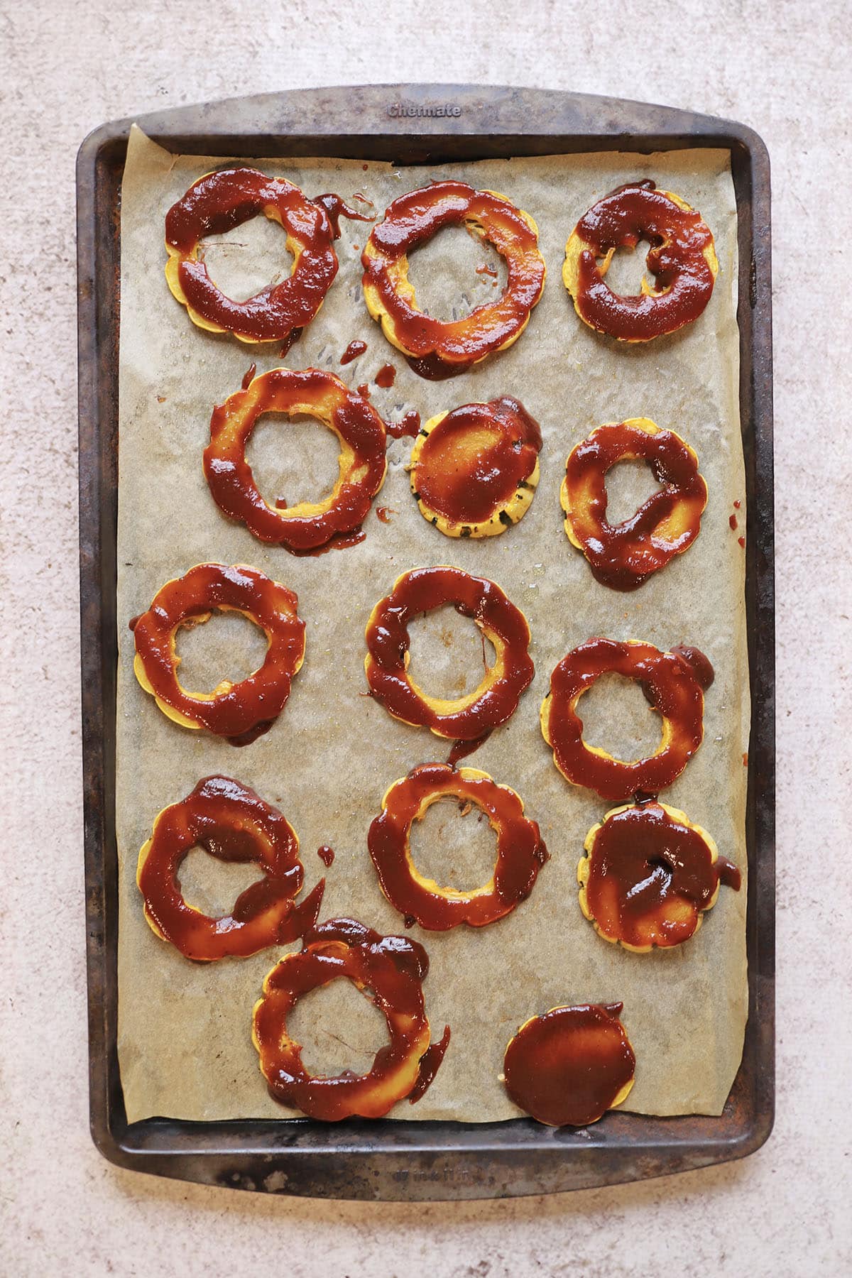 Delicata squash rounds with barbecue sauce on baking sheet.