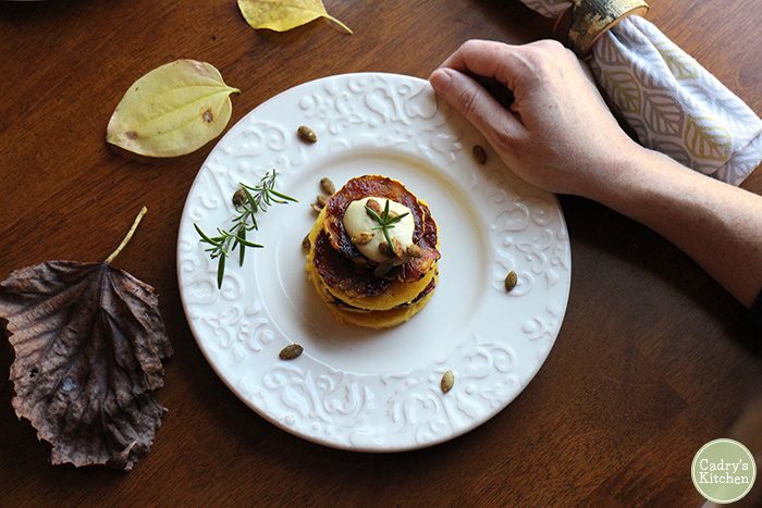 Hand holding plate with circles of polenta, delicata squash, and cashew cream.