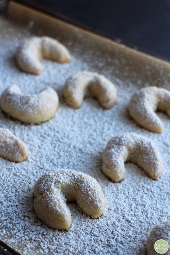 Moon cookies on parchment paper, covered in powdered sugar.