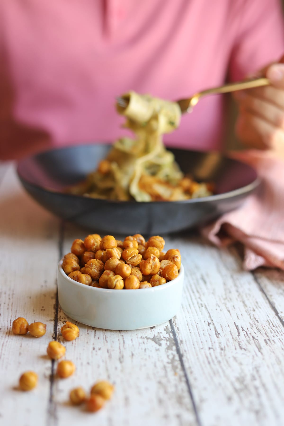 Fried chickpeas on table with bowl of pasta in background.