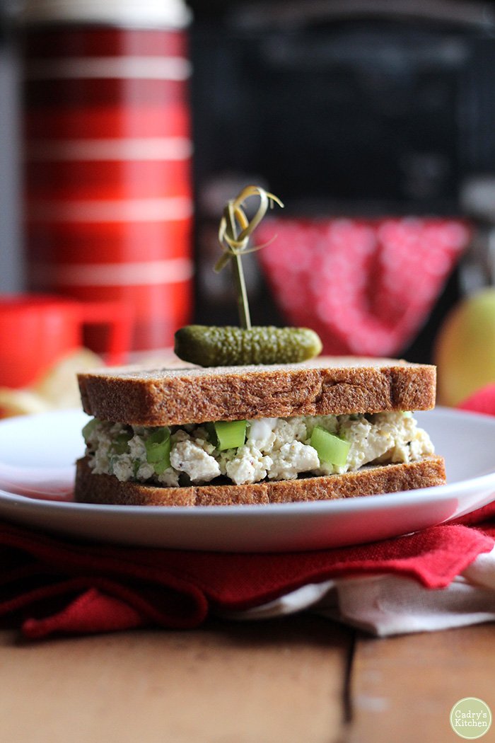 Vegan egg salad sandwich on plate with pickle.