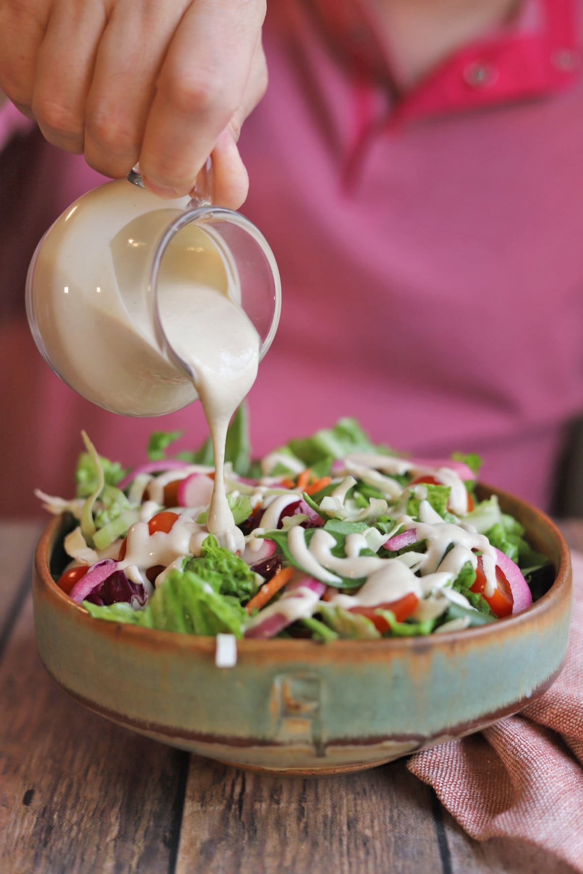 Tahini dressing being poured onto leafy green salad.